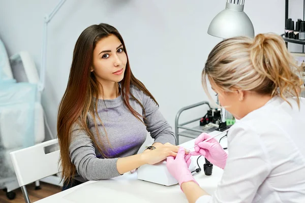 The nail artist draws on the nails of a brunette girl in salon