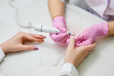 Manikürcü kız çivi bir cihazla parlatır.