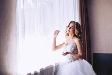 Gelin bir lüks beyaz elbiseli cam kenarında bir odada duruyor