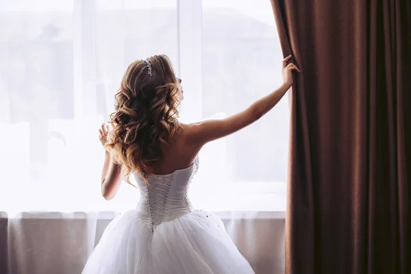 豪華な白いドレスを着た花嫁がカーテンを引く — ストック写真