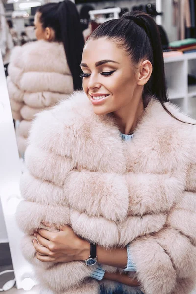 A cute brunette dressed in a pink fur vest in a clothing store