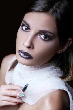 Seksi genç esmer bir şırınga siyah bir sıvı ile onun elinde tutan ve kafasını çevirerek düz, görünüyor.