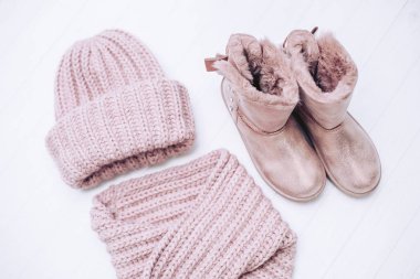 Şık örme kış şapka ve pembe eşarp ile ahşap beyaz zemin üzerinde doğal kürk çizmeler.