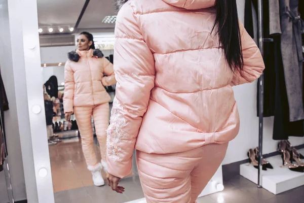 Cute brunette try on pink winter outerwear in a clothing store.