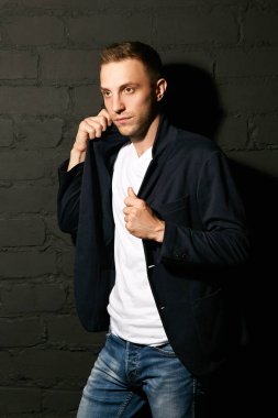 Bir güzel genç mavi bir ceket ve kot gri duvara karşı duruyor ve yakasını düzeltiyor