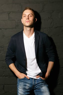 Yakışıklı erkek kot pantolon ceplerinde siyah tuğla duvara yaslanmış ellerini tutar