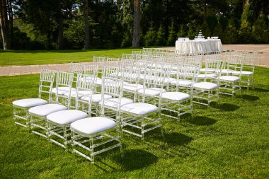 Oturma Konuklar açık havada düğün töreni sırasında. Çimenlikte ağaçlarıyla çevrili şık beyaz sandalye