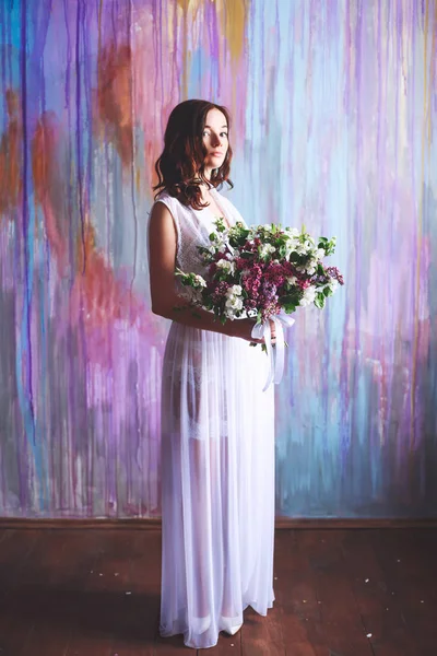 Young bride in a borough dress with a large bouquet of flowers in the early morning on a multi-colored background