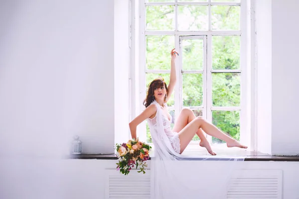 窓辺の花の花束と座ってポーズ ホワイト シャツの若い花嫁 — ストック写真
