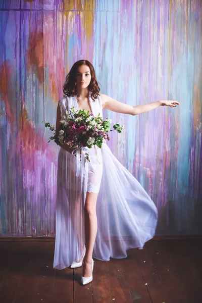 Bride in a borough dress with a large bouquet of flowers in the early morning on a multicolored background