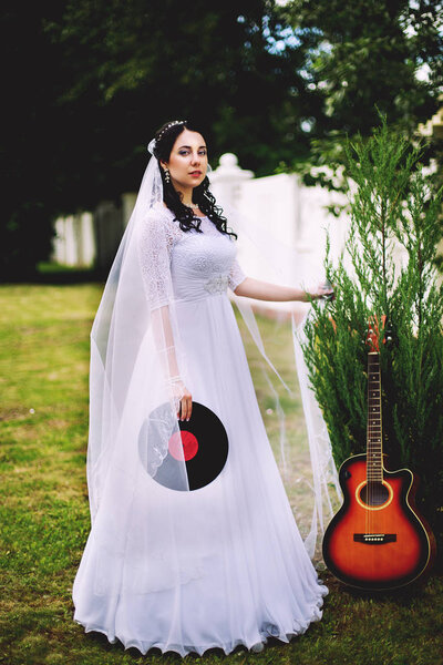 Wedding in musical style. The bride in a white wedding dress outdoors with a guitar