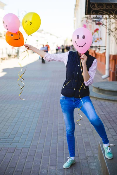 A young girl covers her face with a balloon. A bundle of balloon