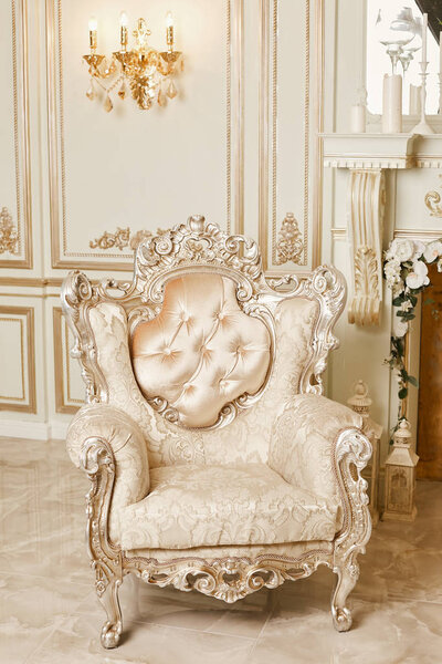 Luxurious expensive classic beige armchair with carved elements stands on a marble floor in an expensive interior