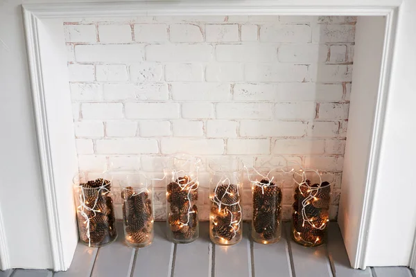 Chimenea decorativa con bombillas de vidrio con conos de abeto y una guirnalda — Foto de Stock
