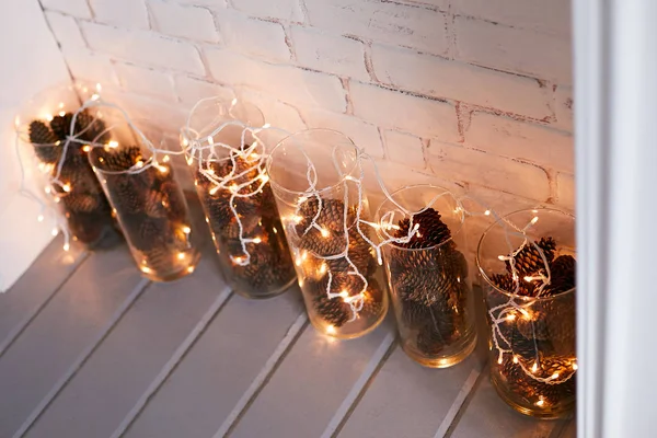 Üveg vázák, fenyő kúpok és fényes füzér a következő látnivaló közelében: fehér téglafal — Stock Fotó