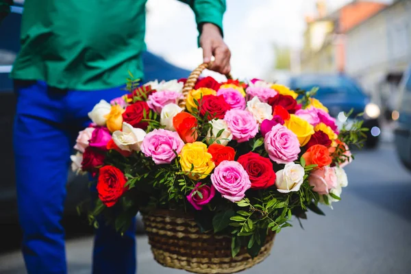 Flower delivery. Man holding a big bouquet of beautiful flowers in a wicker basket