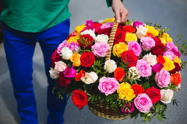 Flower delivery. Man holding a large basket of beautiful multi-colored roses