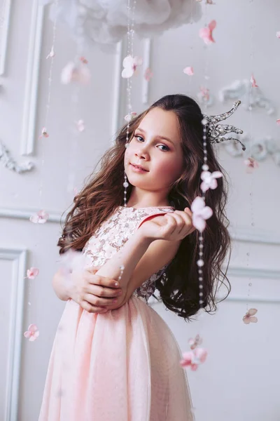 Vacker liten flicka i en fantastisk interiör poserar i en rosa klänning och en krona på huvudet. — Stockfoto