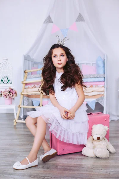 一位身着轻礼服、头戴皇冠的小公主正坐在一个粉红色的手提箱上，沉思地看着一边。豌豆上的公主. — 图库照片