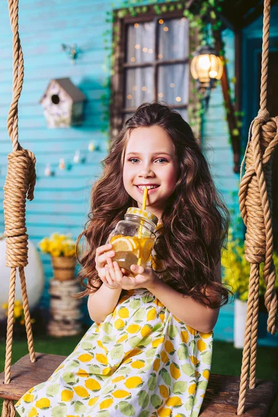 かわいい若い女の子は、村でロープスイングに乗っている間、ジュースを飲み、笑顔. — ストック写真