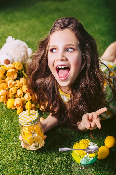 Giovane ragazza allegra beve acqua gassata mentre sdraiato sul prato in una giornata di sole. Celebrazione della luce Pasqua nella natura . — Foto Stock