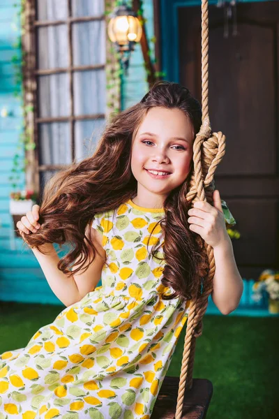 Niño feliz montando en un columpio cerca de la casa. Dulce chica en un vestido . — Foto de Stock