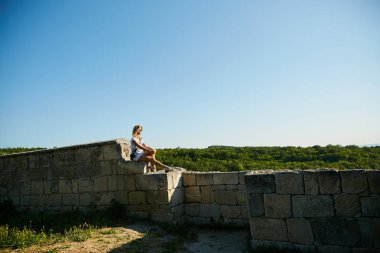 Bir kadın, Kırım yarımadasının manzarasına hayran olan eski bir taş duvarda oturuyor..