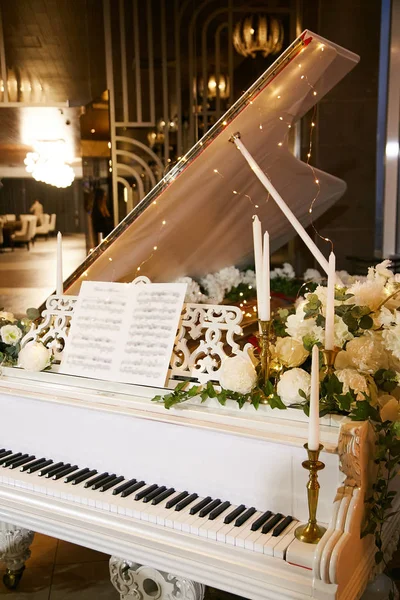 Дорогое белое пианино, украшенное позолоченными подсвечниками со свечами и свежими цветами на свадебной церемонии в ресторане . — стоковое фото