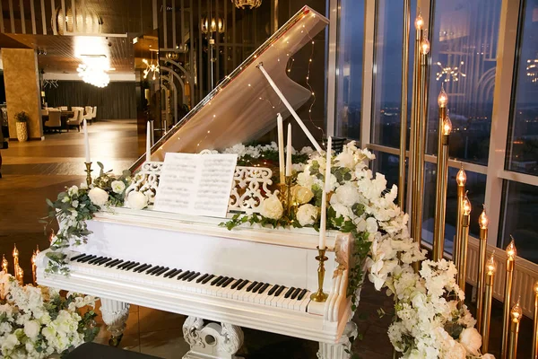 Bir düğün sırasında kapalı restoran. Doğal çiçekler, mumlar ve çelenk ile dekore edilmiş güzel beyaz piyano.