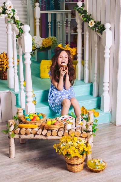 Nettes kleines Mädchen beißt Osterkuchen auf der Treppe sitzend. Feiertags-Ostern. — Stockfoto