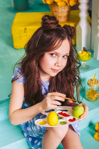 A girl sitting on the steps near the house painted Easter eggs. Cute girl brunette. — Stock Photo, Image