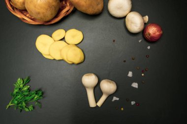 Dilimlenmiş patates, yeşillik, soğan, siyah arka planda sarımsak.