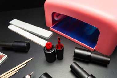 Siyah arka planda manikür ve pedikür için bir takım kozmetik aletler. Jel cilası ve lamba.