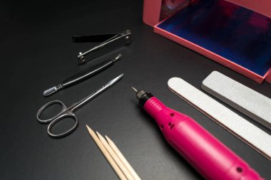 Siyah arka planda manikür ve pedikür için bir takım kozmetik aletler. Jel cilası, tırnak törpüsü, meme uçları, lamba, değirmen makası.