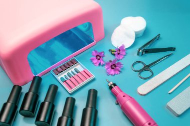 Mavi arka planda manikür ve pedikür için bir takım kozmetik aletler. Jel cilası, tırnak törpüsü, maşa ve lamba..