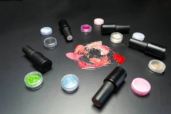 Gel polishes of different colors poured on a black background, gel polishes in bottles and decorative spangles