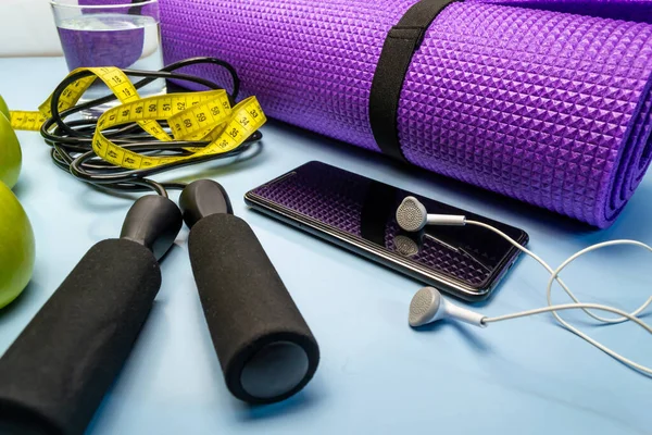Yoga mat and glass of water close-up. Sports equipment, green apples and a jump rope.