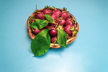 Tam hasır çilek tabağı ve bir kırmızı kiraz, mavi arka plan.