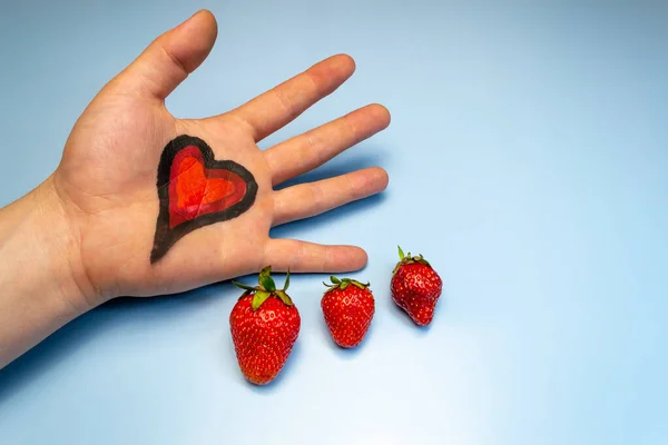 A heart is drawn on the hand, three strawberries on a blue background