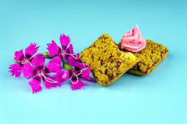 Üzerinde pembe şekerlemeler olan buğday ekmekli kurabiyeler ve üstünde pembe küçük çiçekler, mavi arka plan.