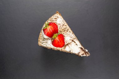Çilekle süslenmiş üçgen bir tiramisu parçası. Siyah arkaplan