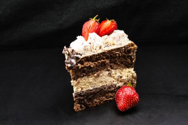 Çilekle süslenmiş üçgen bir tiramisu parçası. Siyah arkaplan