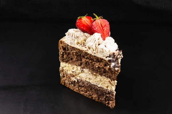 Çilekle süslenmiş üçgen bir tiramisu parçası. Siyah arkaplan