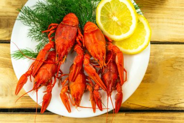 Dereotu ve limonla süslenmiş beyaz bir tabakta kaynamış kerevit, ahşap arka plan.