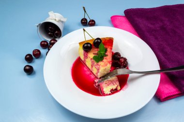 Hafif kahvaltı. Bir çatal, nane ve kirazla süslenmiş beyaz bir tabakta bir parça güveç kırdı. Kirazlı beyaz kova. Mavi arkaplan