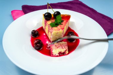 Hafif kahvaltı. Bir çatal, nane ve kirazla süslenmiş beyaz bir tabakta bir parça güveç kırdı. Kirazlı beyaz kova. Mavi arkaplan