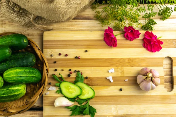 Kesme tahtasının üzerinde salatalık, sarımsak ve otların yanında iki dilim doğranmış yeşil salatalık var. Ahşap arkaplan
