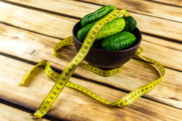 Cucumbers in a brown plate and a centimeter tape. Wood background