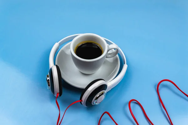 Cup of coffee and white headphones on a blue background
