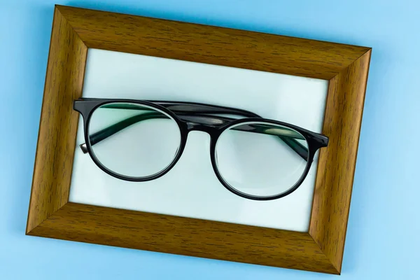 Round glasses in black frames lie in a photo frame. Blue background